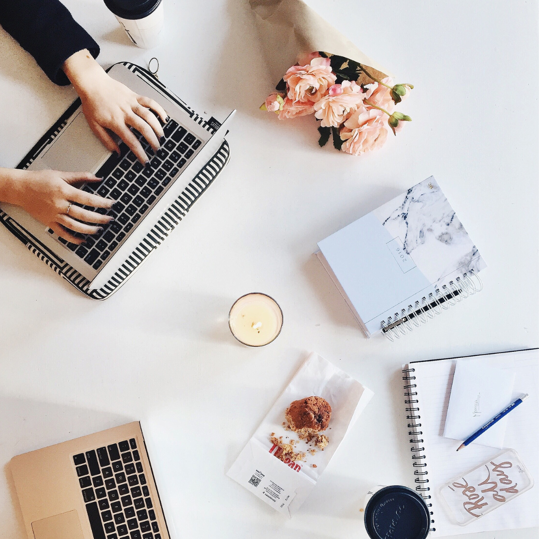 Picture of laptop with a notebook, coffee, flowers, and a notebook